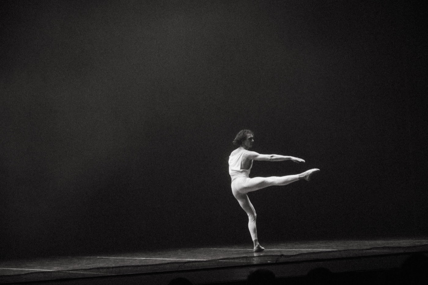 Dancer extending one leg across a dark stage